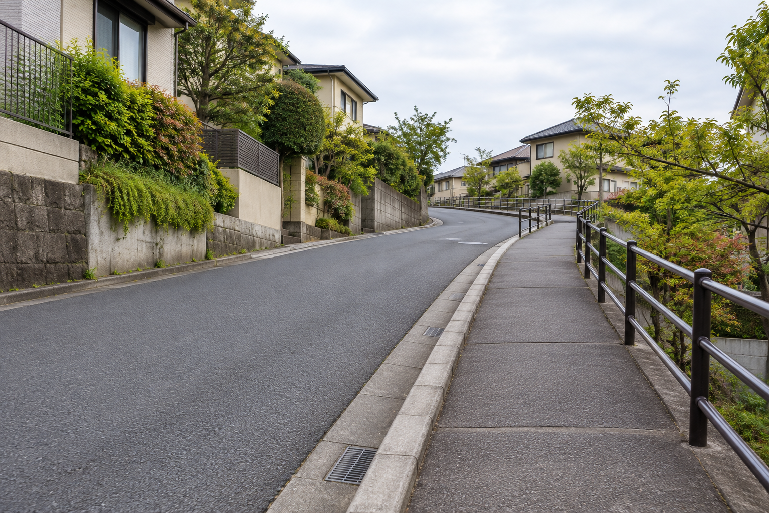 緩やかな坂道に沿って歩道と手すりが続く住宅地